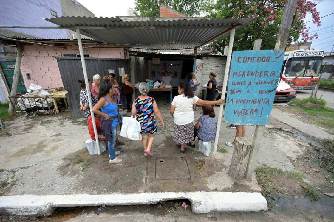 People queue to leave their bags with empty plastic containers at a soup kitchen to receive a free meal