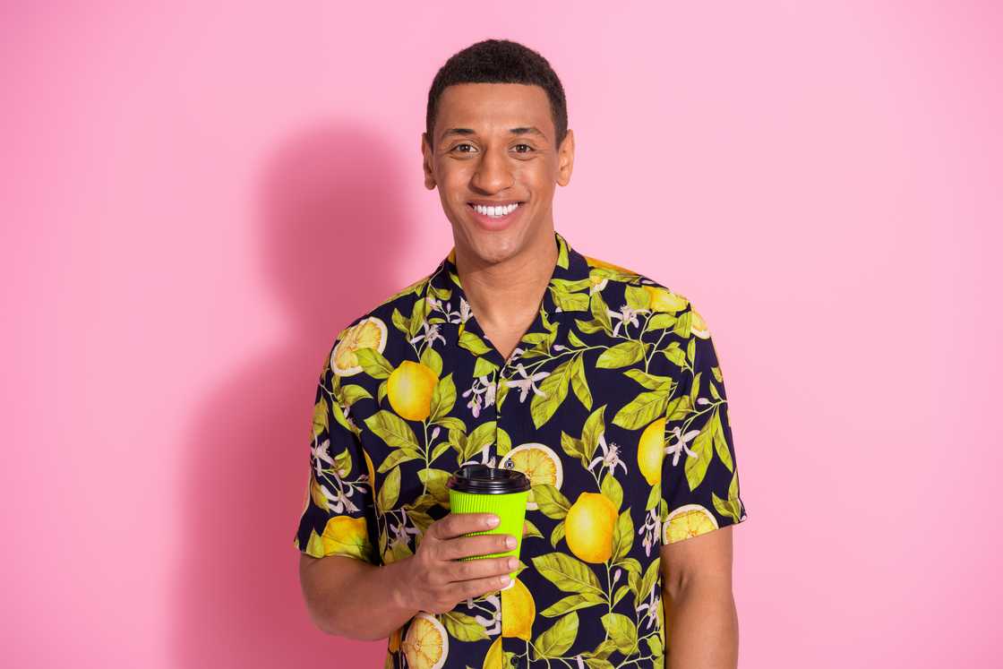 A man wearing the Hawaiian shirt, standing in a pink background.