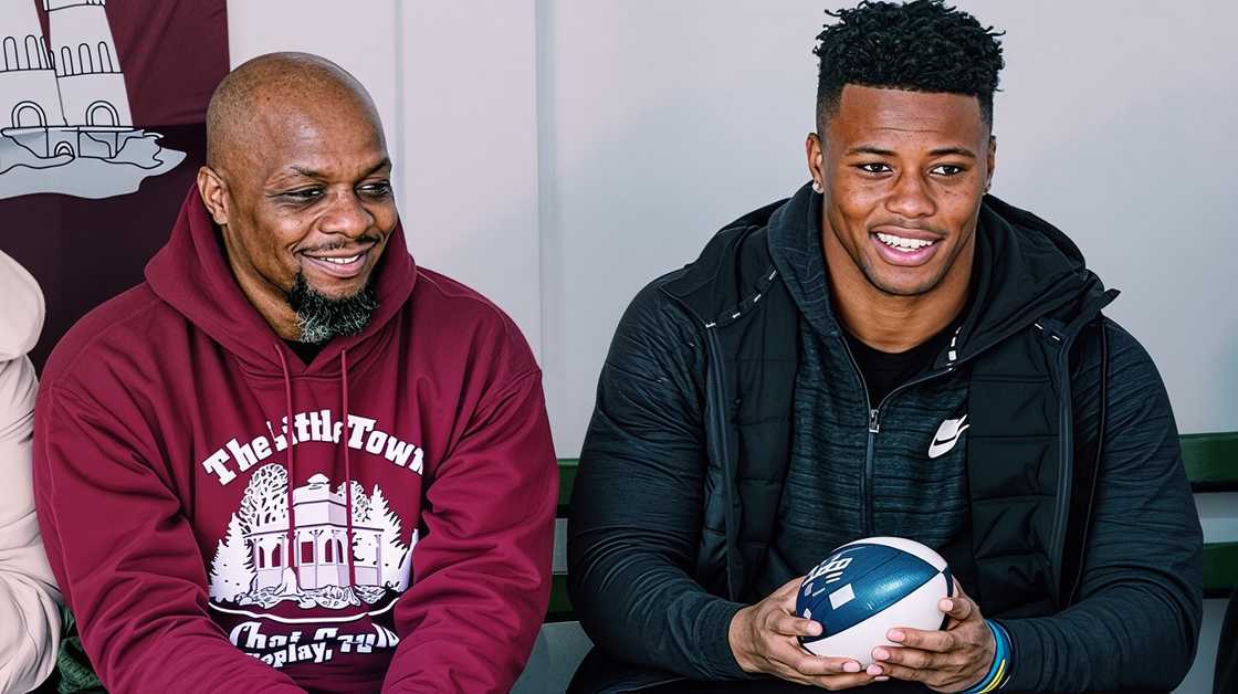 Saquon Barkley holds a football while sitting with his father, Alibay Barkley