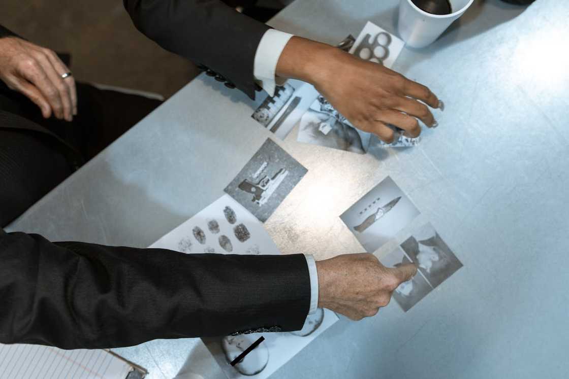 Investigators examining photographs and fingerprint evidence on a table. Investigators examining photographs and fingerprint evidence on a table.
