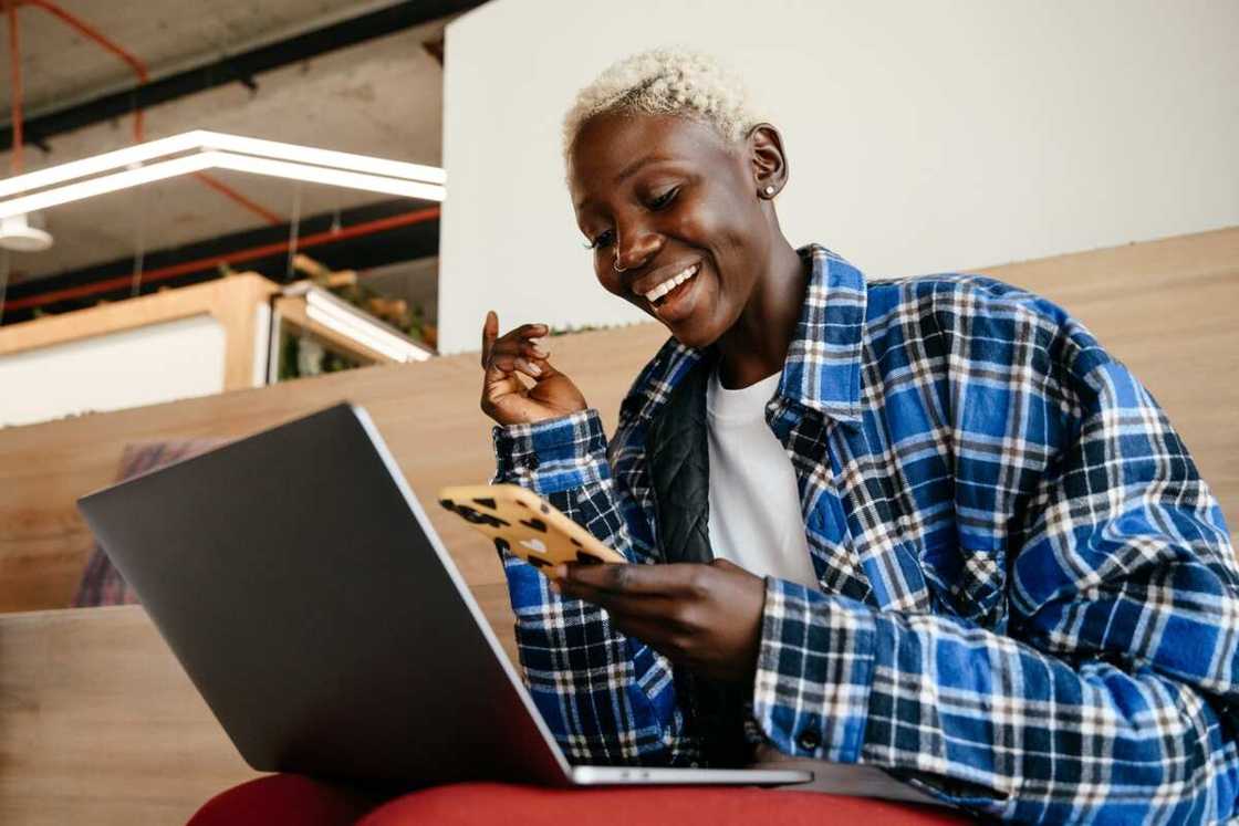 A woman with blonde hair and a blue checkered shirt with a smartphone and a laptop