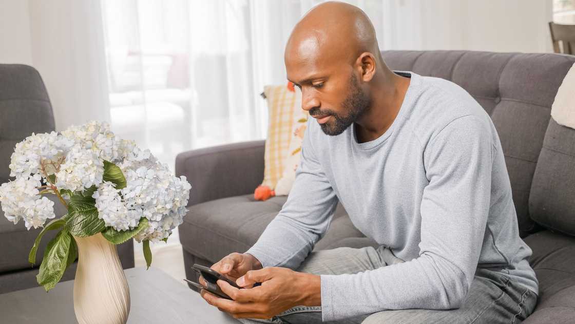 A man sitting on a grey couch as he uses a smartphone