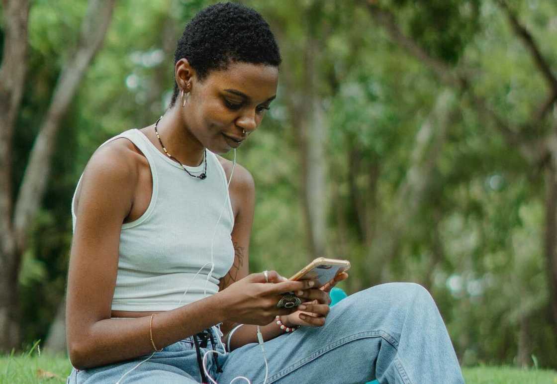 A lady using a phone while sitting on the grass