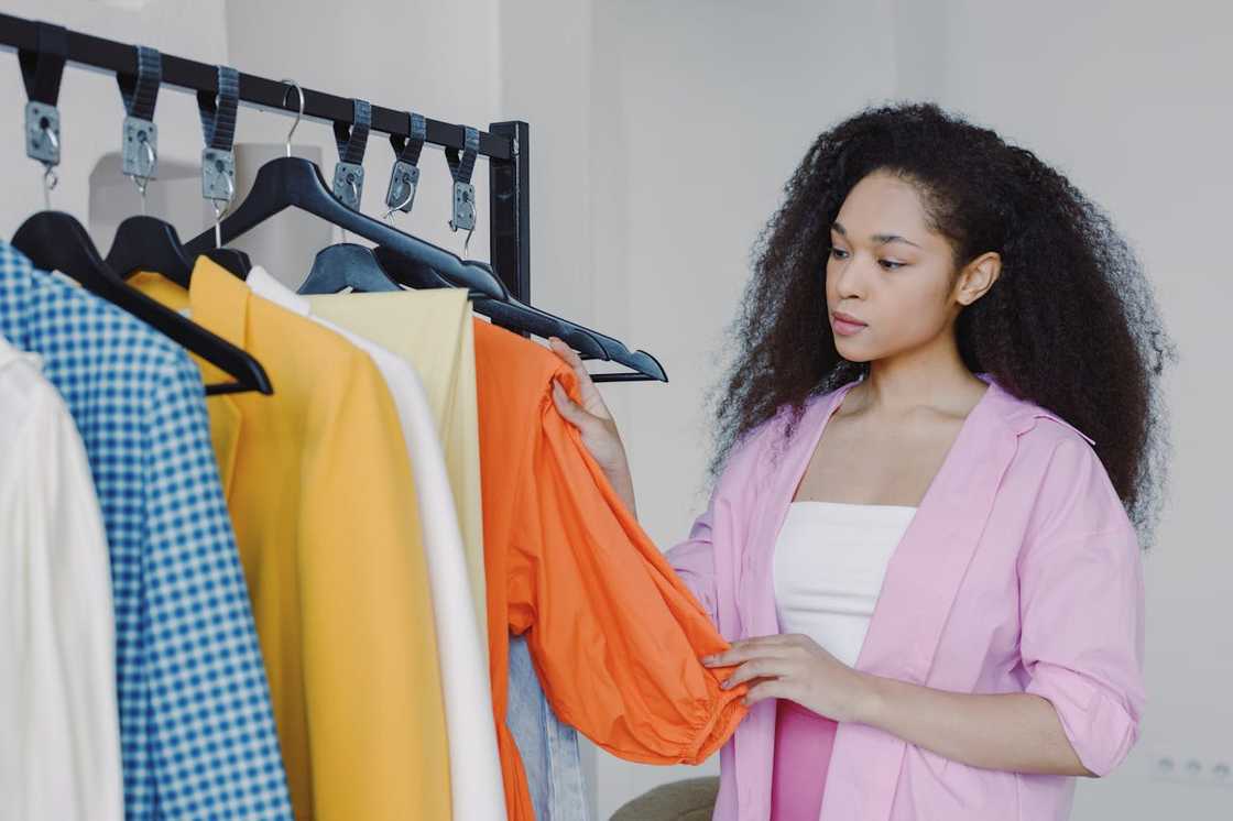 A woman examines a bright orange blouse on a clothing rack. A woman examines a bright orange blouse on a clothing rack.