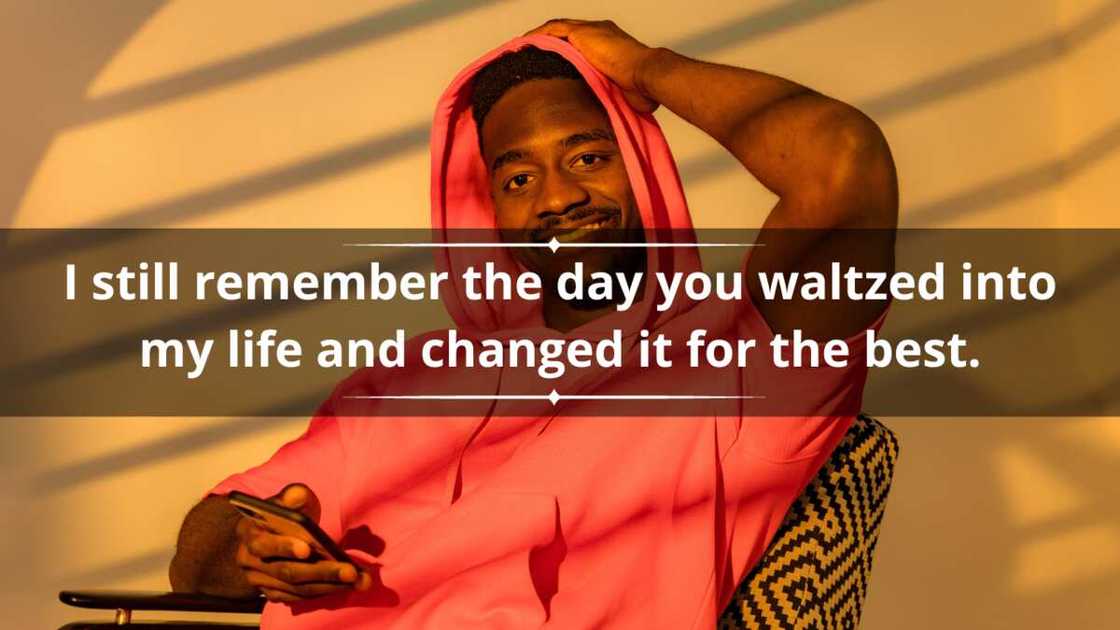 A man wearing a red hoodie smiles while sitting on a chair and holding a smartphone A man wearing a red hoodie smiles while sitting on a chair and holding a smartphone