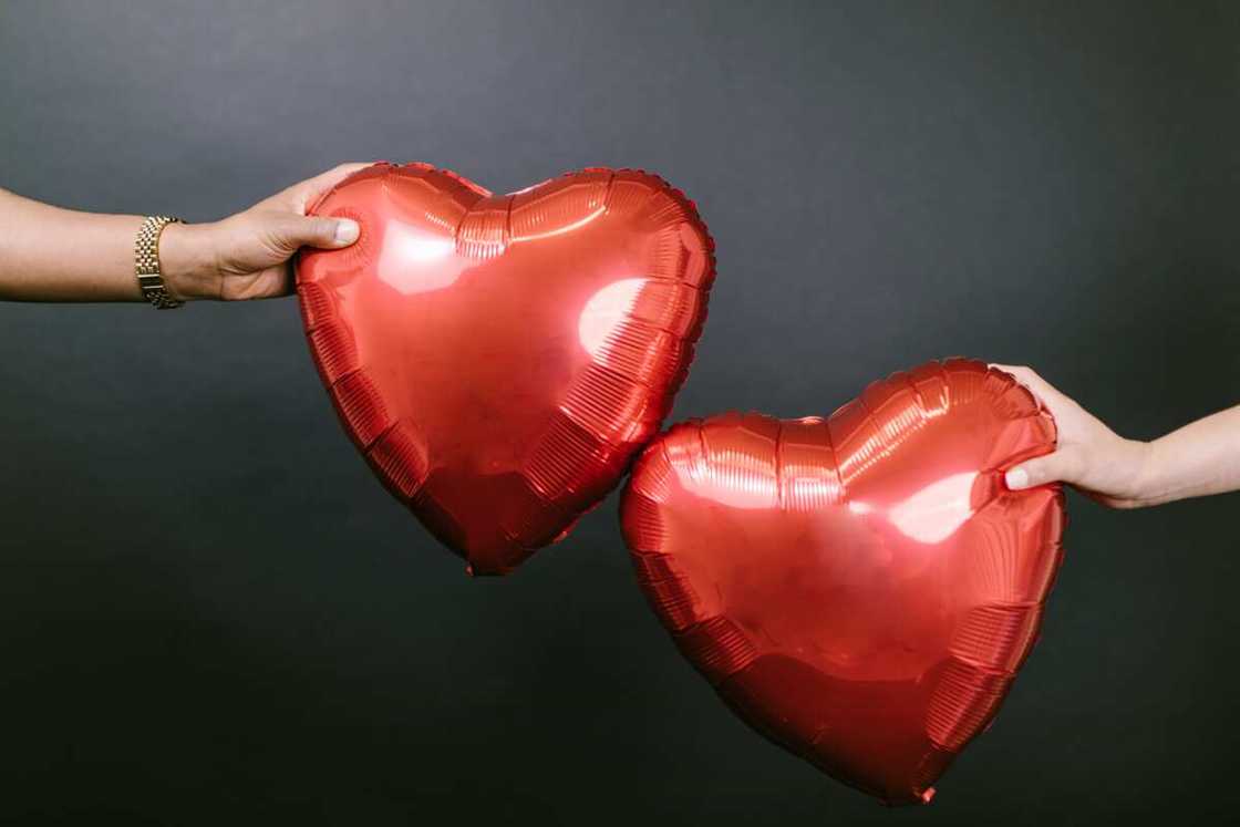 Two people holding two red heart-shaped balloons