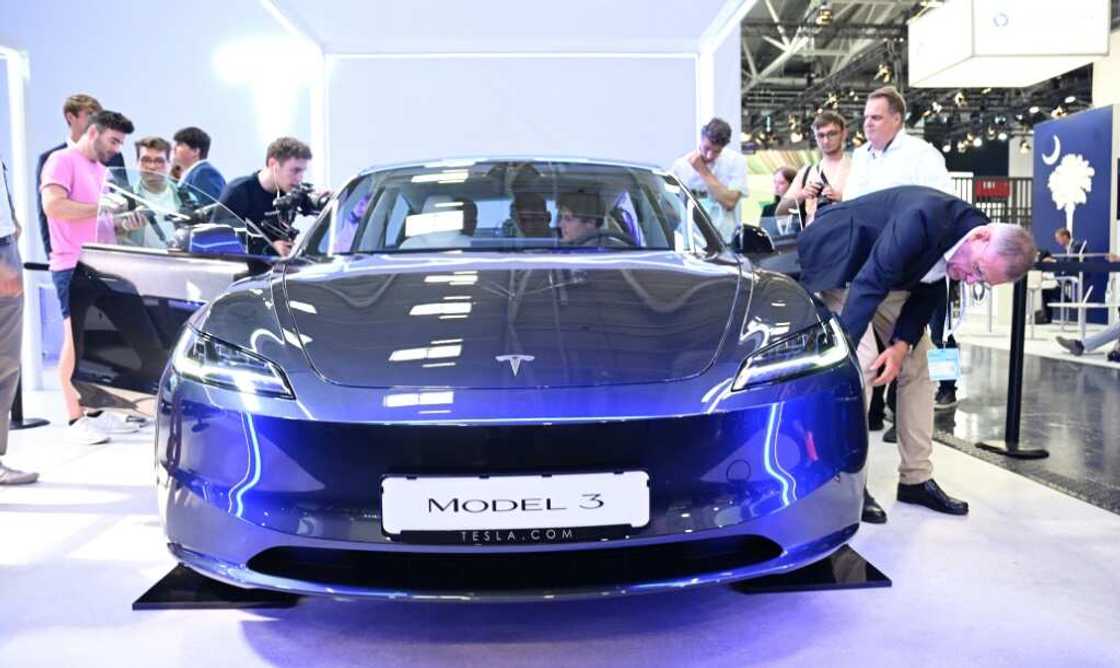 Visitors inspect a Tesla model 3 car on display at the International Motor Show held in Munich, southern Germany, on September 4, 2023