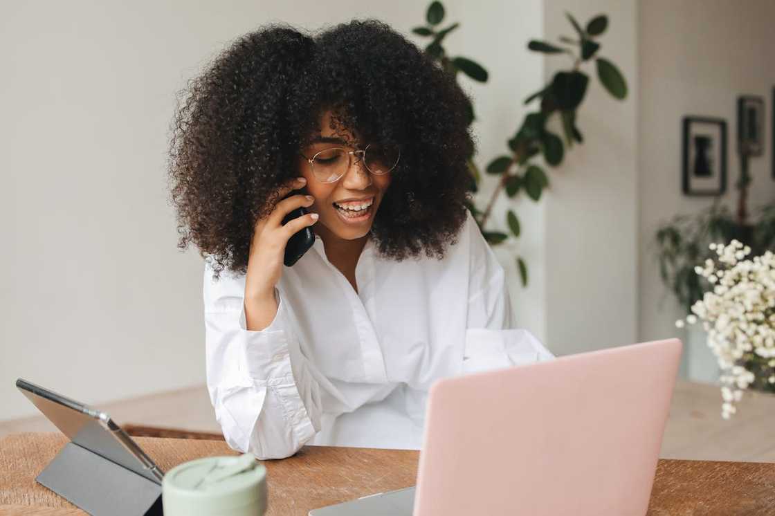 A smiling woman talking on the phone while working on a laptop.