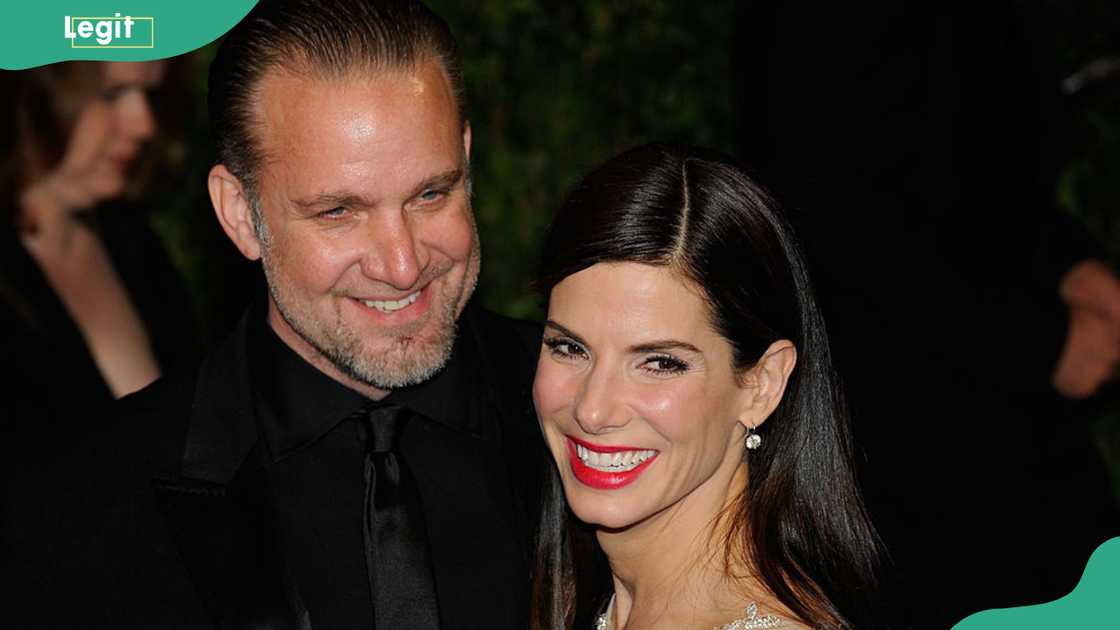 Jesse James in a black suit and Sandra Bullock in a sparkly gold gown smiling cheek to cheek at the camera at the 2010 Vanity Fair Oscar Party in West Hollywood