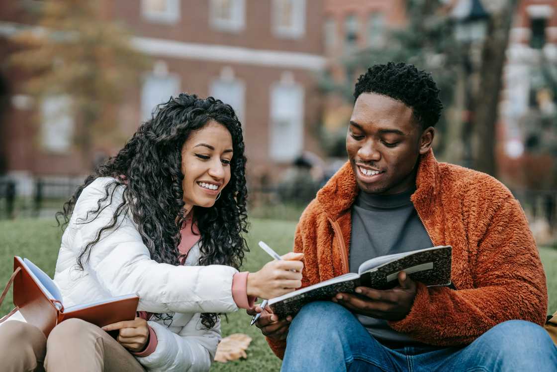 A young woman and man are studying together on a grass lawn