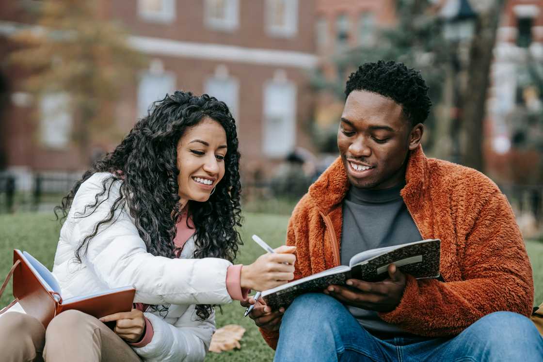 A young woman and man are studying together on a grass lawn A young woman and man are studying together on a grass lawn
