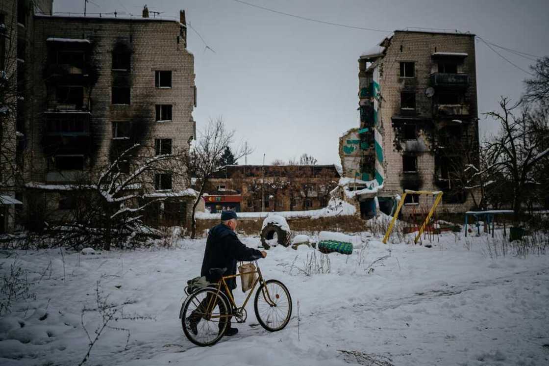 A resident of Borodianka pushes his bike on a snow covered street next to destroyed residential buildings A resident of Borodianka pushes his bike on a snow covered street next to destroyed residential buildings