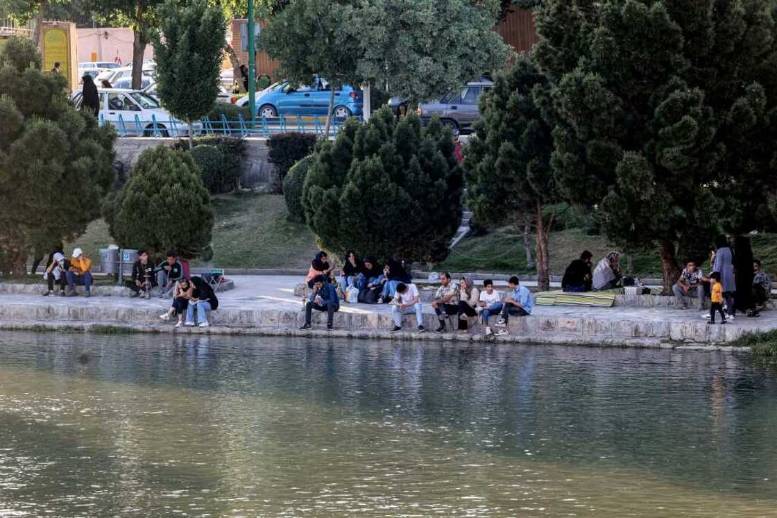 A file picture shows people sitting along the bank of the Zayandeh Rood river on May 15, 2022 in Iran's central city of Isfahan -- the river has been drying out, but families seek out riversides and other cooler areas to relax during the summer