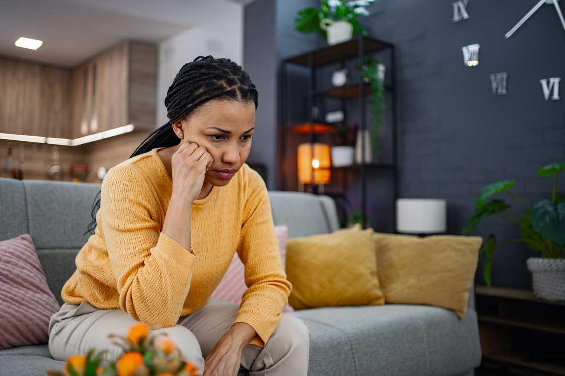 A sad woman sitting on sofa at home feeling down