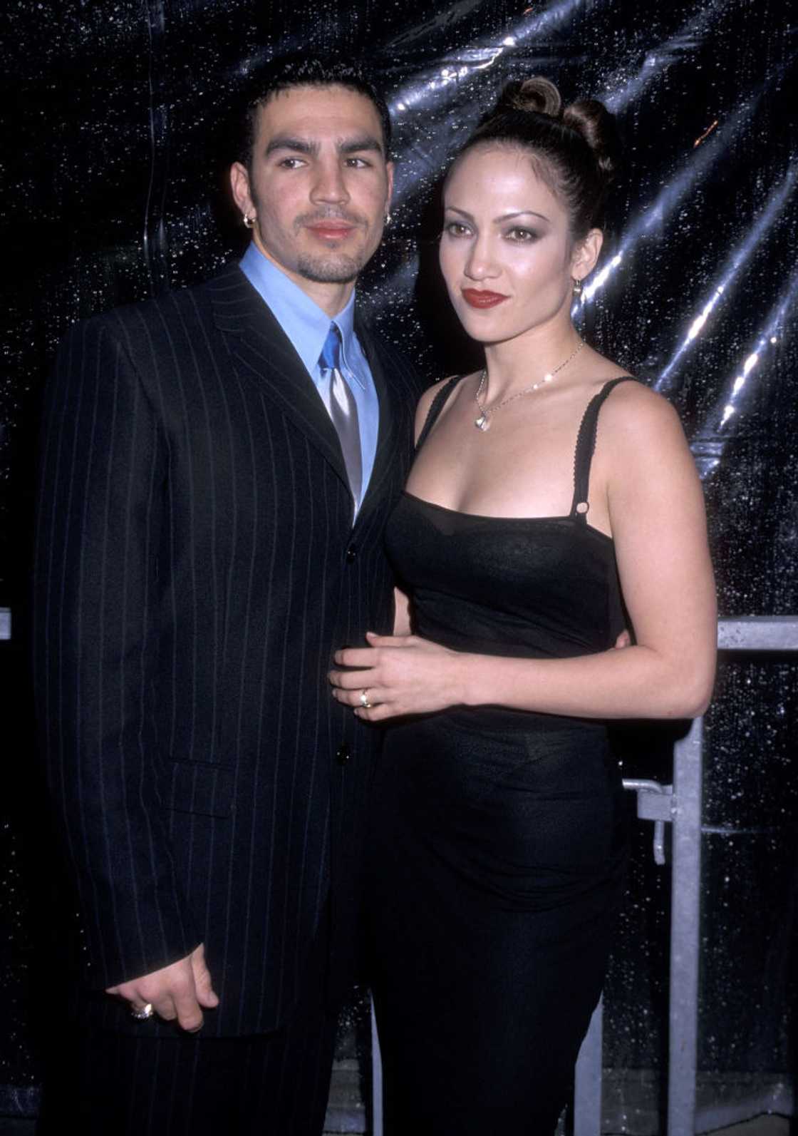 A man in a pinstriped suit and a woman in a black slip dress with her hair in a bun posing together. A man in a pinstriped suit and a woman in a black slip dress with her hair in a bun posing together.