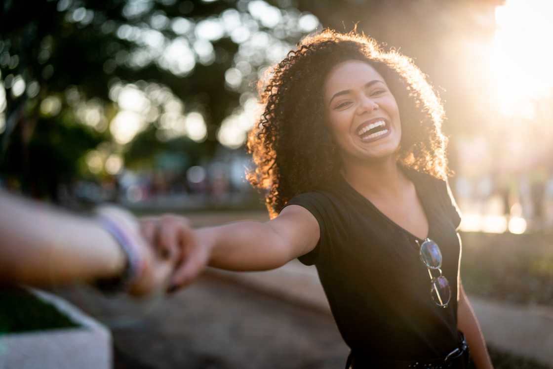 A happy woman with a curly hair holding her boyfriend's hand