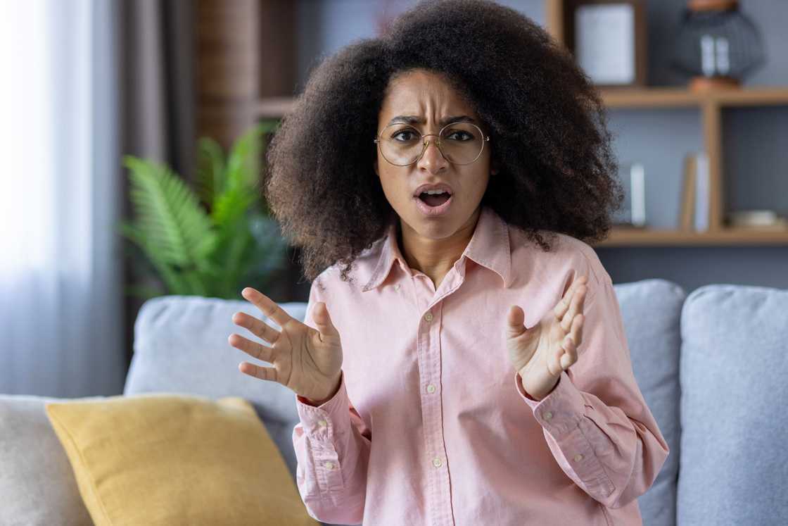 Surprised woman with curly hair and glasses sitting on a couch at home