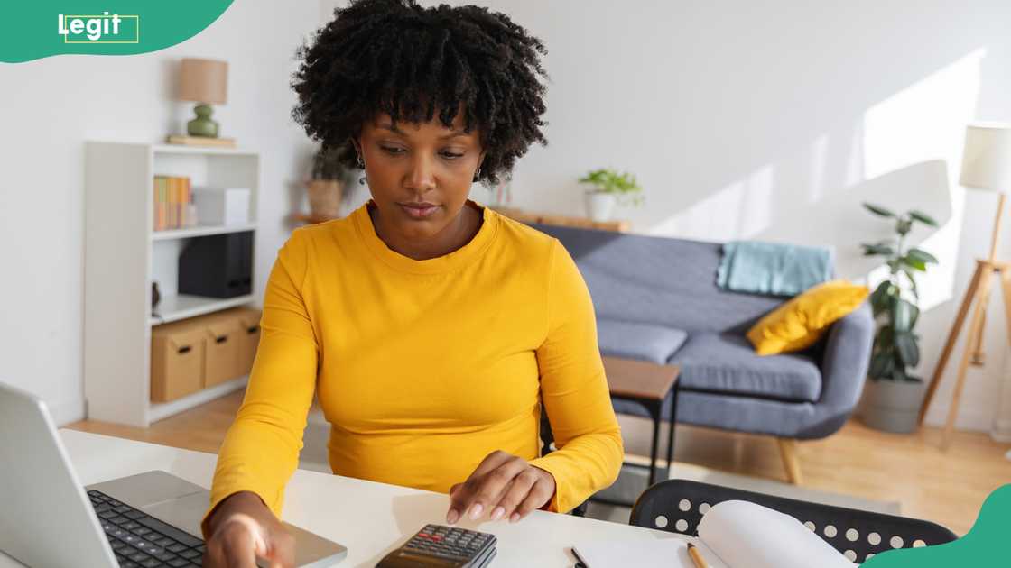 A young woman using a calculator and a laptop.