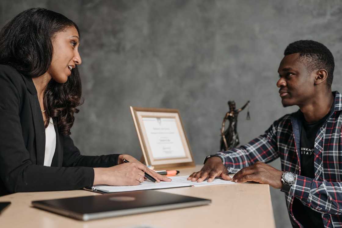 A woman and a man sit across a desk discussing documents.