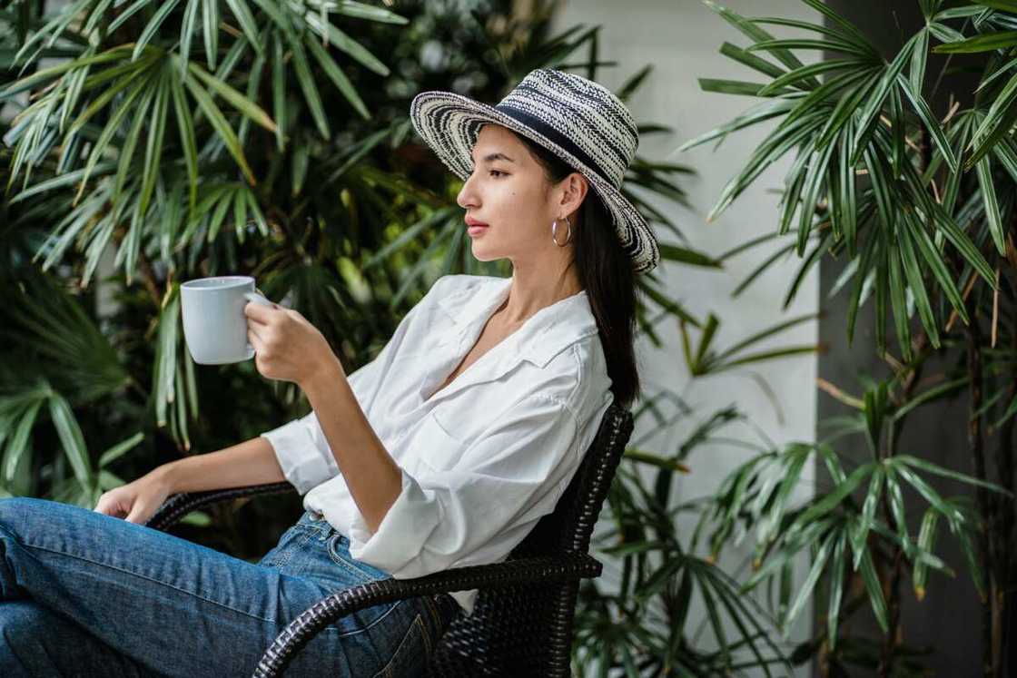 A young female in blue jeans and a white shirt holding hot beverage while resting in an armchair A young female in blue jeans and a white shirt holding hot beverage while resting in an armchair