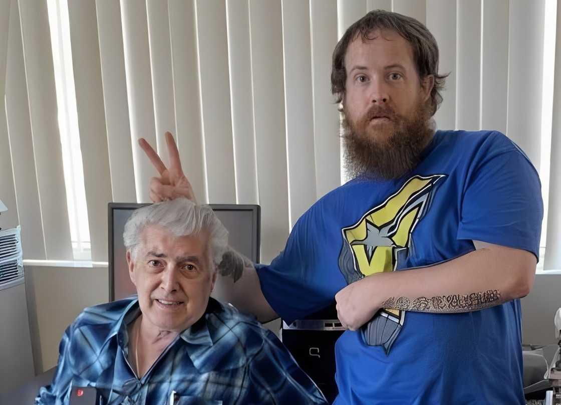 Randy Barker is seated on an office chair (L), and his grandson Brandt Barker is posing for a photo standing next to him (R)