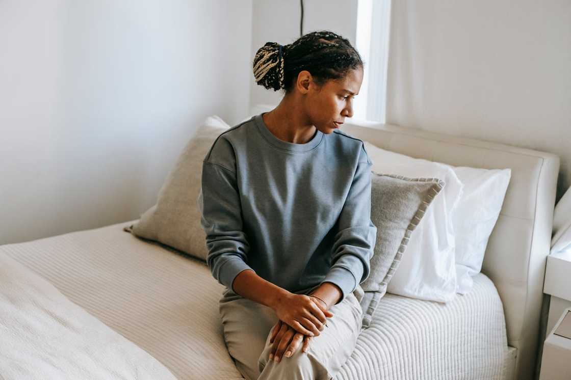 A woman sits on the edge of her bed, deep in thought.