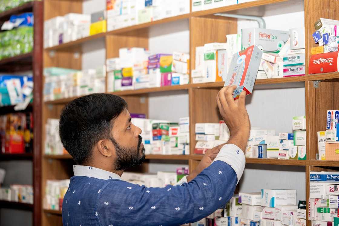 A man reaches for a box of medicine on a pharmacy shelf.