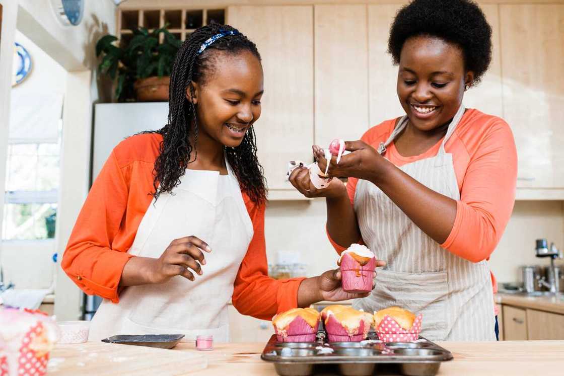 Two happy girls having fun icing cupcakes in the kitchen at home.