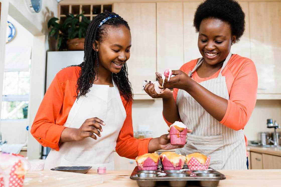 Two happy girls having fun icing cupcakes in the kitchen at home. Two happy girls having fun icing cupcakes in the kitchen at home.
