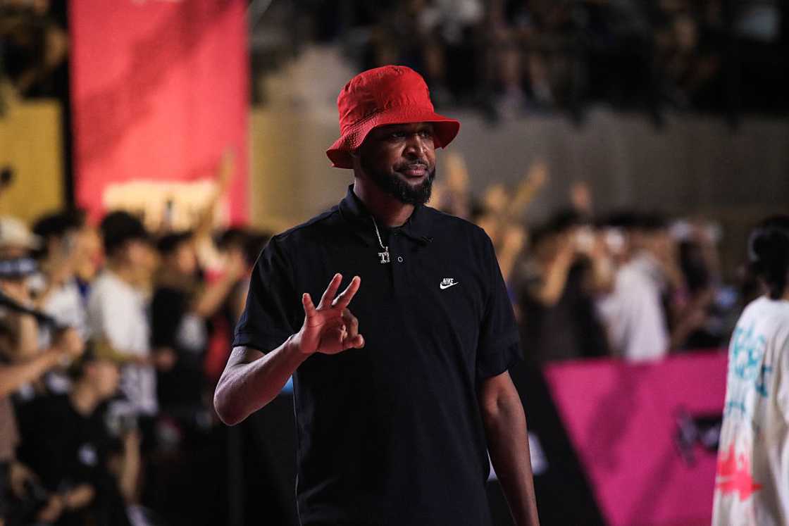 Tee Morant in a red bucket hat and black polo shirt making a hand gesture toward the camera at a basketball masterclass in Shanghai, 2025