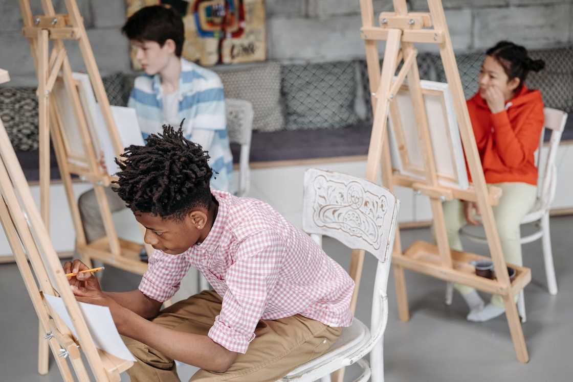 Students sit at easels, drawing in an art class.