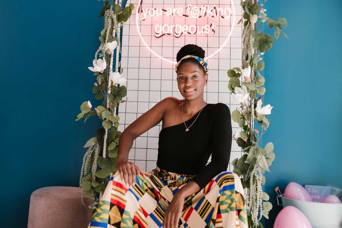 A smiling woman sits beneath a neon sign during a photoshoot. A smiling woman sits beneath a neon sign during a photoshoot.