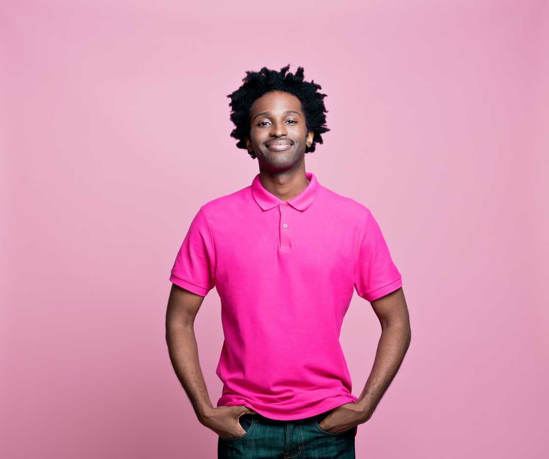 A young man wearing a pink polo shirt with his hands in his pockets