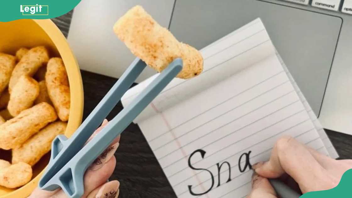 A person writing in a notebook while snacking from a Snactiv hands-free holder A person writing in a notebook while snacking from a Snactiv hands-free holder