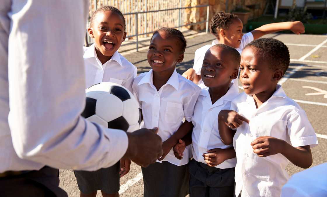 A teacher hands young pupils a ball. A teacher hands young pupils a ball.