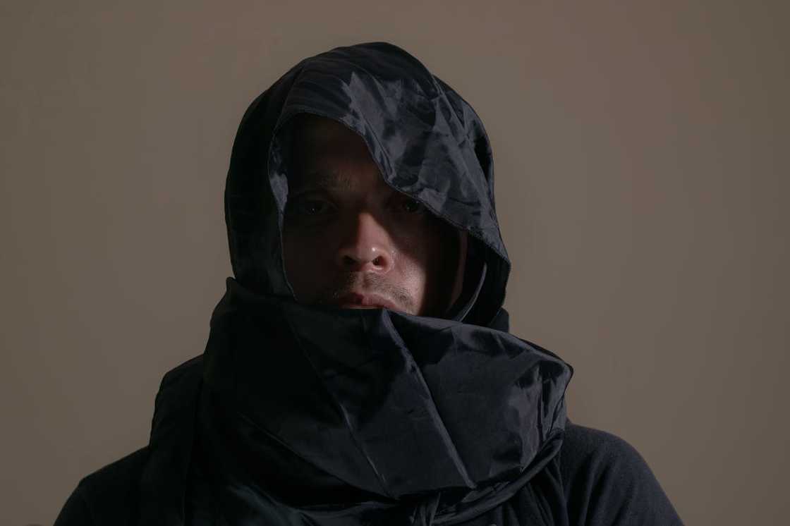 A man wearing a dark hooded jacket in low lighting.
