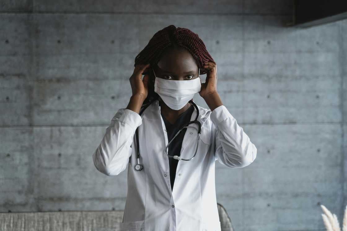 A female doctor in a white coat wearing a white face mask