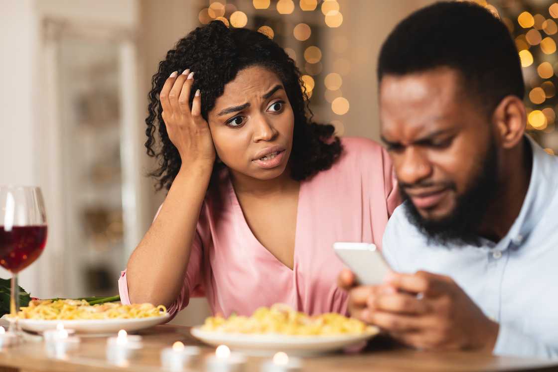 An angry woman looking at her boyfriend stuck on his smartphone.