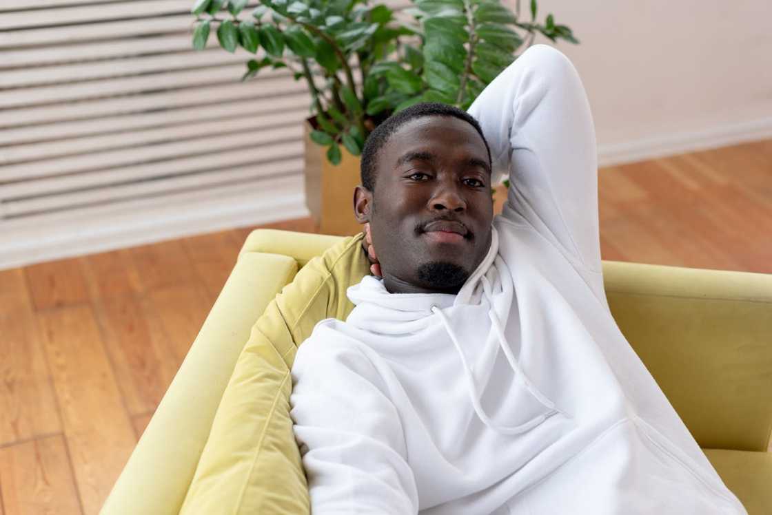 A man in a white hoodie relaxes on a sofa with his arm behind his head.
