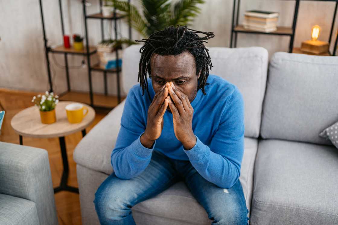 A close-up of tired hands wiping tears in a dimly lit room.