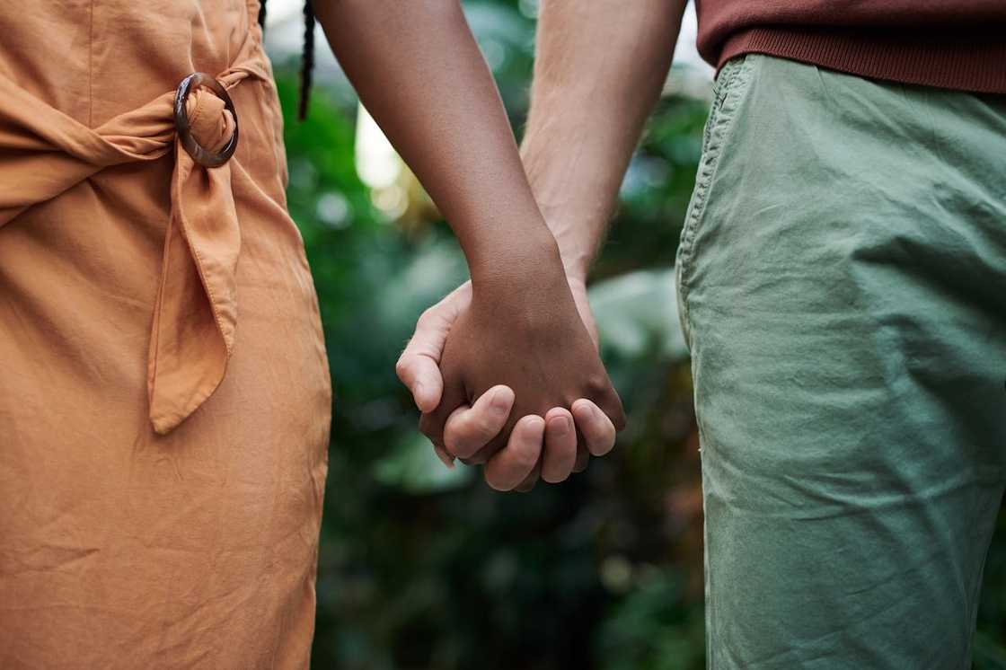 A couple hold hands while standing outdoors. A couple hold hands while standing outdoors.