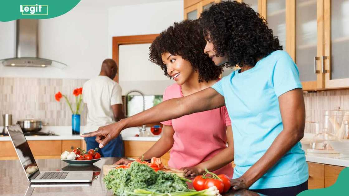 Two women referring to a recipe on a laptop in kitchen