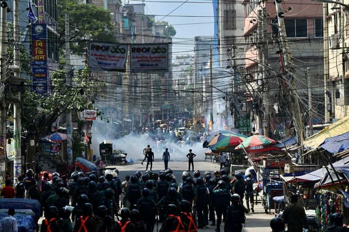 Bangladesh police (foreground) stand guard clashes with garment workers (top)demanding higher wages
