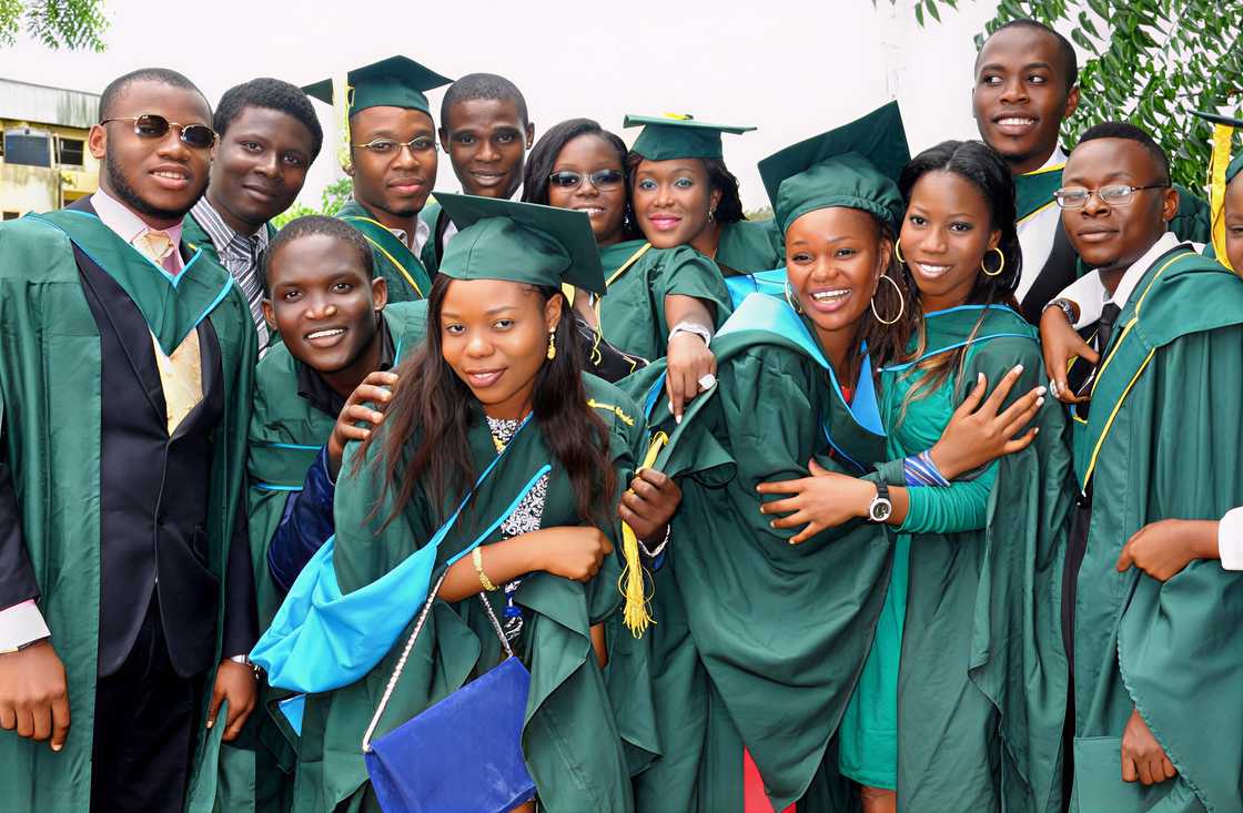 Students in academic robes and mortarboard caps pose during their graduation
