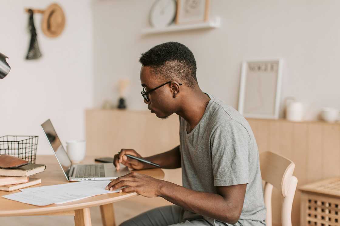 A man in a grey tee is using a laptop on a wooden desk A man in a grey tee is using a laptop on a wooden desk