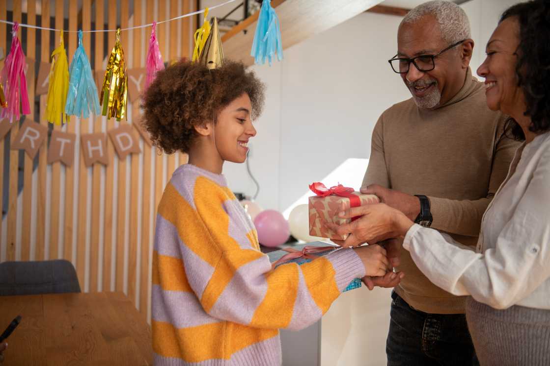 An older couple giving a wrapped present to a smiling teenage girl on her birthday An older couple giving a wrapped present to a smiling teenage girl on her birthday