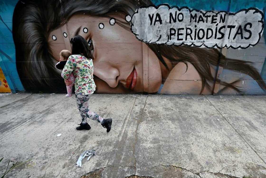 A woman holding a baby walks past a mural reading 'Stop killing journalists' in Mexico City