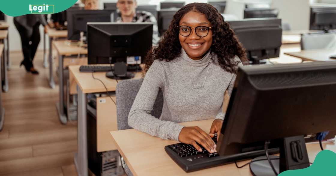 A young cybersecurity student poses in class in front of a computer A young cybersecurity student poses in class in front of a computer