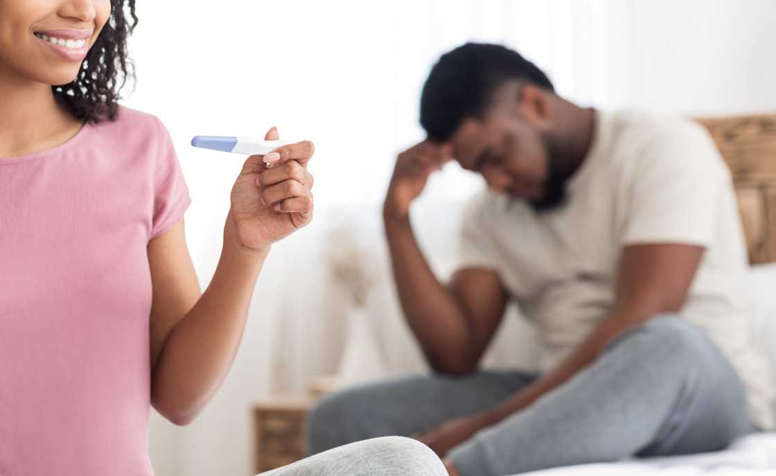 A happy woman with a pregnancy test and an upset man A happy woman with a pregnancy test and an upset man