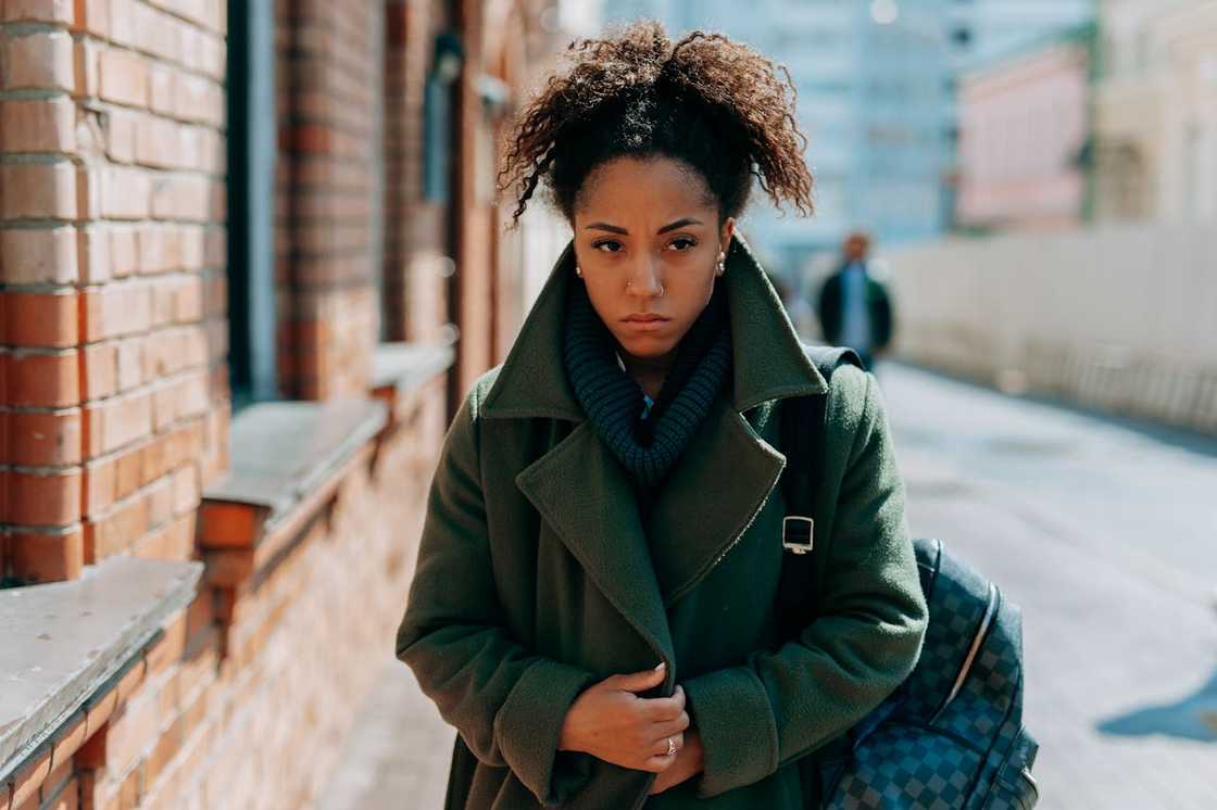 Woman walking outdoors with a serious expression, wearing a coat and carrying a bag. Woman walking outdoors with a serious expression, wearing a coat and carrying a bag.